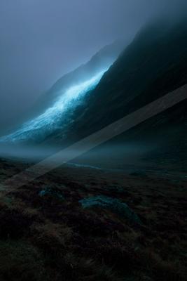 A dramatic mountain valley shrouded in thick fog, featuring a glowing blue-white glacier cascading down a dark mountainside, with a foreground of purple heather