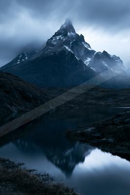 A dramatic landscape of mountains, lake, reflection.