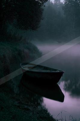 A small dark rowboat is moored at the edge of a calm lake, its reflection visible in the still water, surrounded by thick morning fog and dark trees.