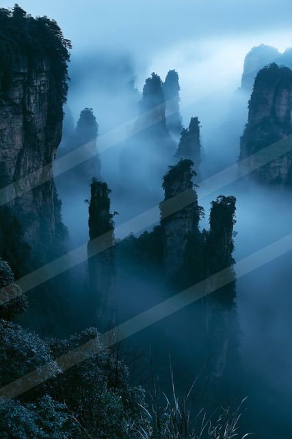 A serene landscape of towering mountain peaks shrouded in mist and fog.