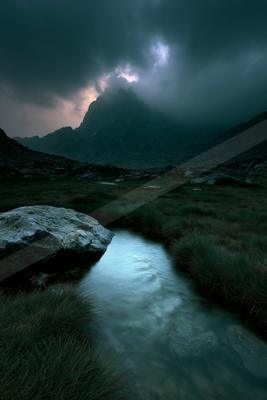 A black-toned moody photograph of valley, volcano, mountain tent.