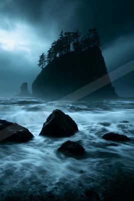 A large rocky island topped with dark trees rises from a turbulent sea with white-capped waves and foreground rocks under a moody, overcast sky.