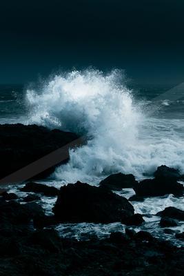 A moody high contrast water scene of an ocean waves, rocks.