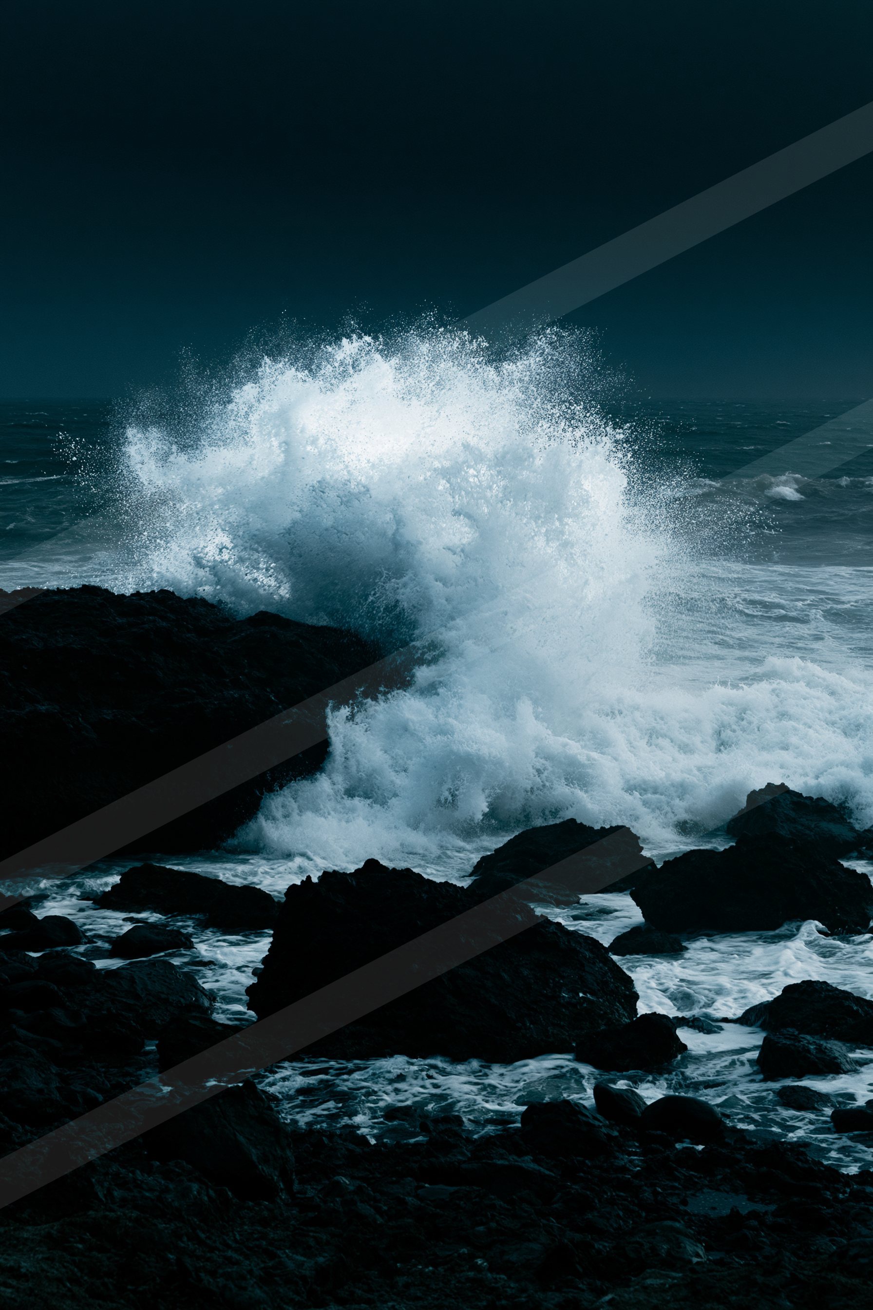 A powerful wave crashes against dark rocky formations under a starless night sky, creating a dramatic spray of white foam.