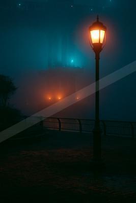 A black-toned moody photograph of spotlight, traffic light, pole.
