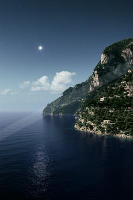 A steep rocky coastline covered in green vegetation and scattered buildings rises above a calm dark sea under a starry night sky with a bright moon and clouds.