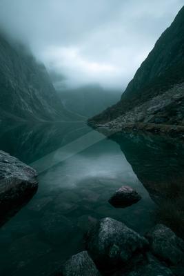 A serene long exposure water scene of lake, mountains, fog.
