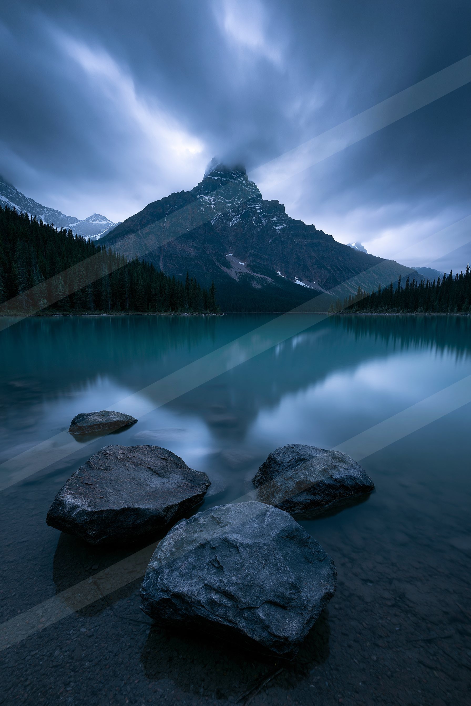 A tranquil lake mirrors a towering mountain peak under a moody sky.