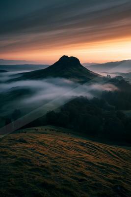 A moody landscape of mountains, valley, field.