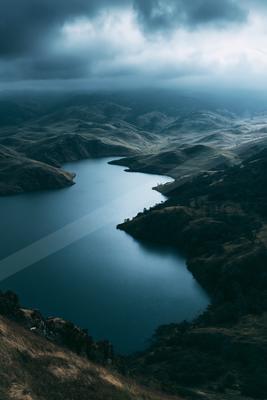 A moody landscape of valley, lake, mountains.