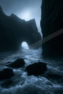 A black-toned moody photograph of promontory, cliff, seashore.