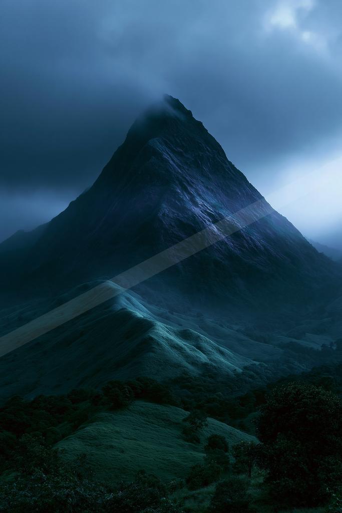 A sharp rocky mountain peak rises through thick fog and dark clouds under a deep blue twilight sky, with rolling green hills and trees in the foreground.