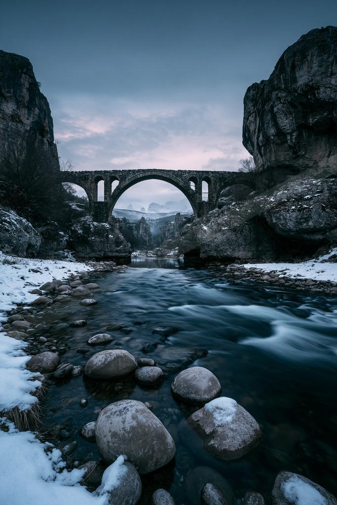 A black-toned moody photograph of valley, seashore, steel arch bridge.