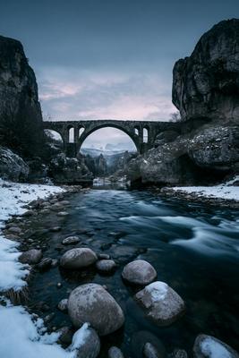 A black-toned moody photograph of valley, seashore, steel arch bridge.