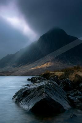 A black-toned moody photograph of lakeside, volcano, valley.
