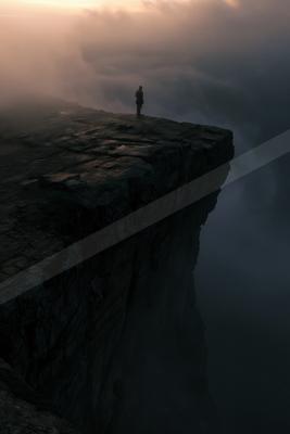 A lone person stands silhouetted on the edge of a steep rocky cliff overlooking a vast sea of clouds during sunset.