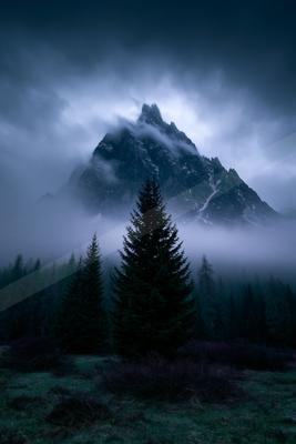 A night landscape of mountains, trees, fog.