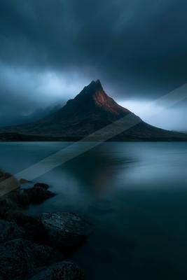 A black-toned moody photograph of volcano, lakeside, promontory.