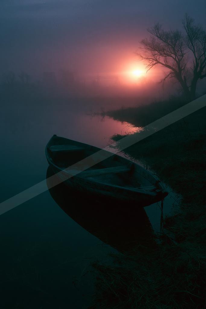 A wooden rowboat rests on the foggy bank of a calm river at sunrise, with a glowing red sun and silhouetted bare trees in the background.