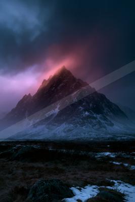 A rugged, snow-dusted mountain peak rises sharply against a dramatic twilight sky filled with swirling pink and dark blue clouds.