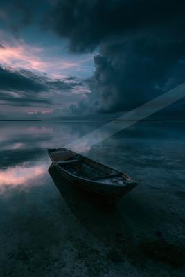 A black-toned moody photograph of canoe, lakeside, seashore.
