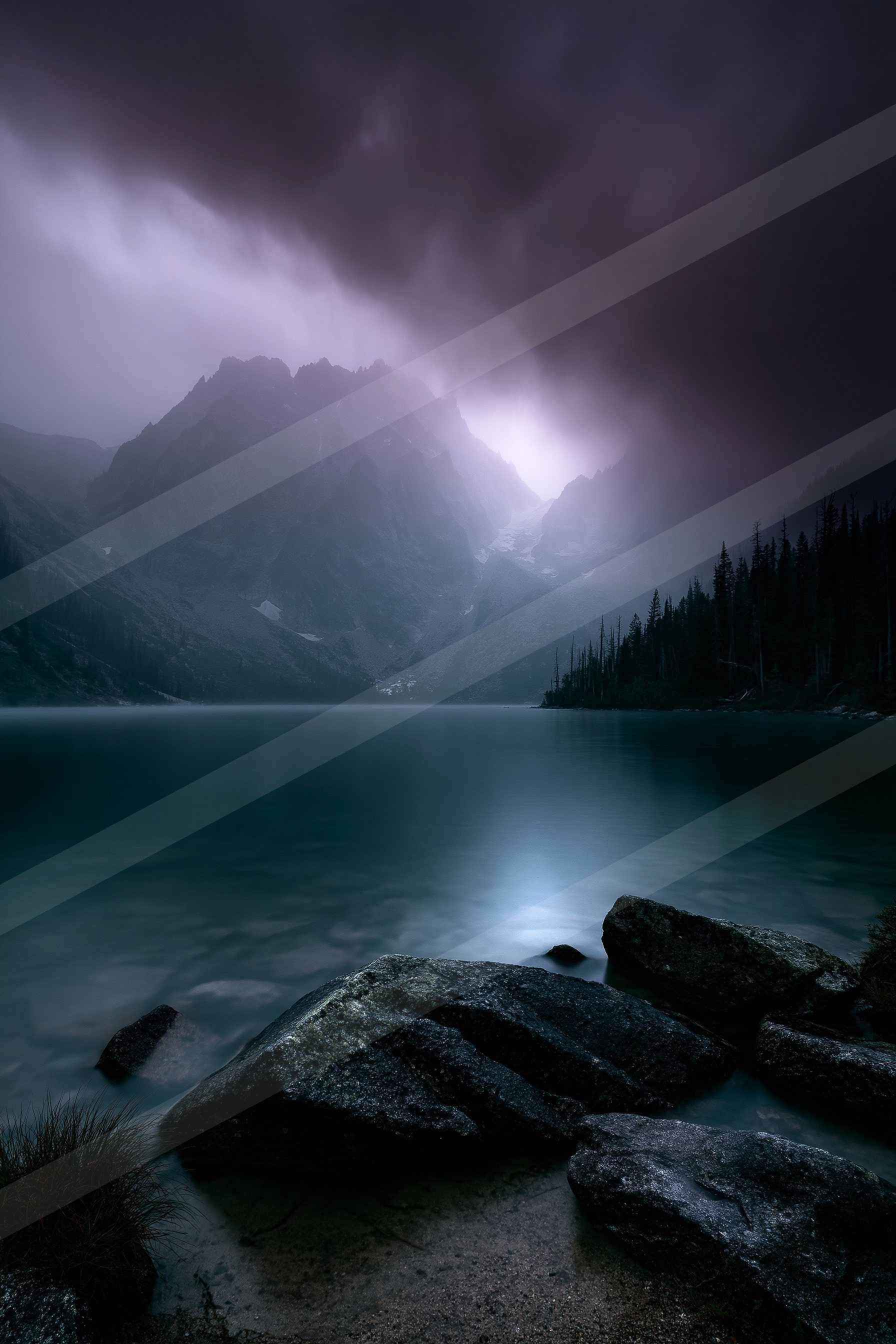A serene lake reflects the dark storm clouds above, framed by rugged mountains and rocky foreground.