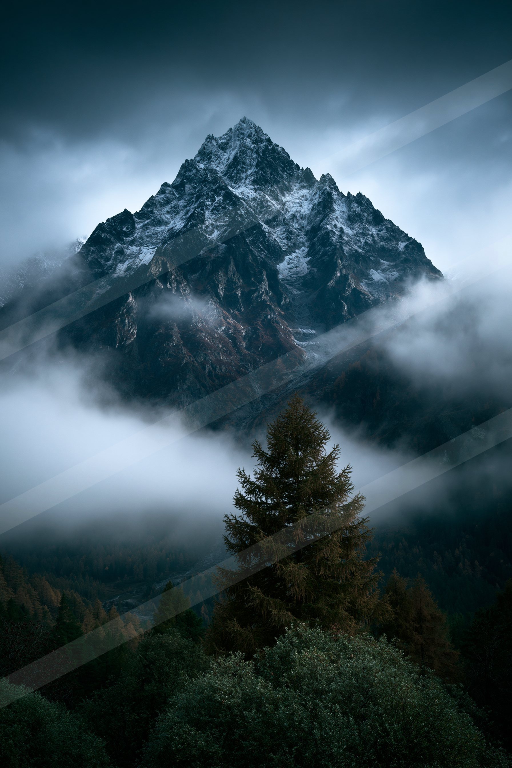 A towering snow-capped mountain peak rises above a dense forest shrouded in mist, with clouds swirling around its base.