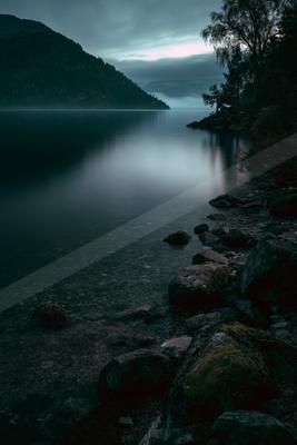 A black-toned moody photograph of lakeside, promontory, volcano.