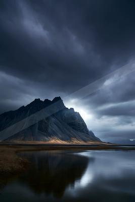 A moody landscape of mountains, lake, storm.