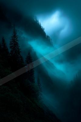 A blue hour landscape of mountains, storm, forest.