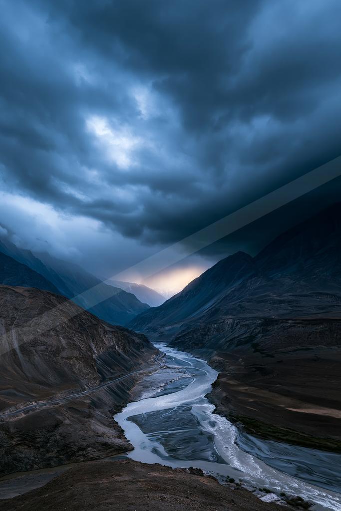 A green-toned moody photograph of valley, dam, suspension bridge.