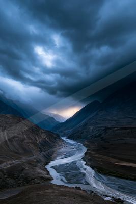 A green-toned moody photograph of valley, dam, suspension bridge.