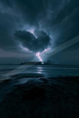 A black-toned moody photograph of seashore, promontory, beacon.
