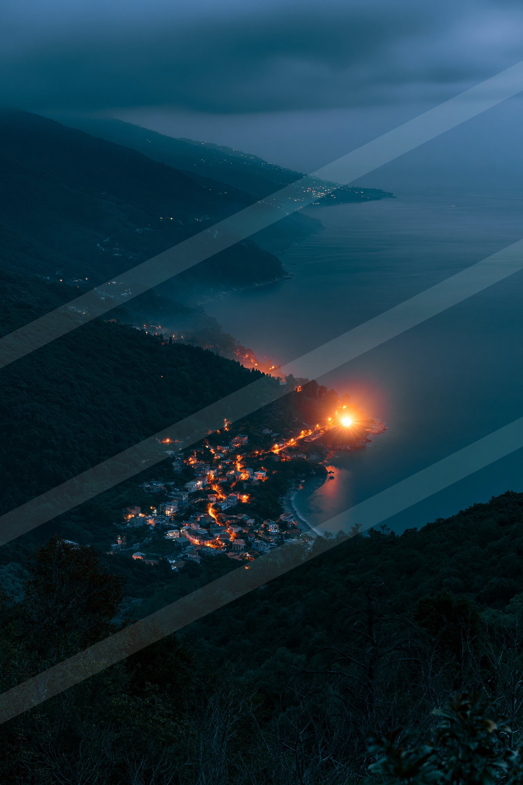A serene coastal village nestled between mountains and the sea, glowing warmly under a dark sky.