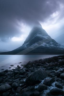 A dramatic landscape of mountains, lake, storm.