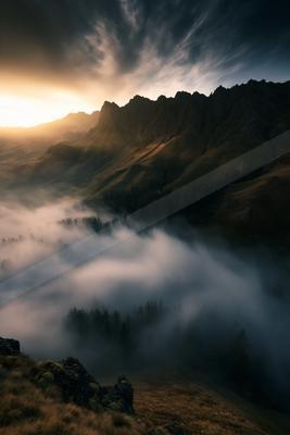 A stunning mountain range bathed in the golden light of sunrise, with a dense layer of mist covering the valley below.