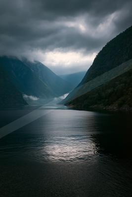 A serene fjord surrounded by towering mountains under a moody, overcast sky.
